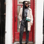 Woman in a beige trench coat, blue jeans, and ankle boots standing on a Parisian street. This photo captures the essence of classic French girl style, highlighting the trench coat as a key element of Parisian chic. The image emphasizes timeless fashion and effortless elegance.