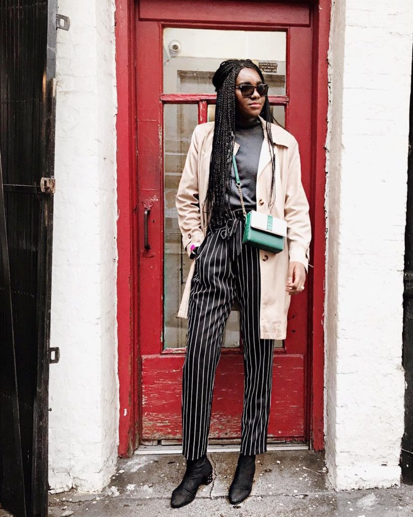 Woman in a beige trench coat, blue jeans, and ankle boots standing on a Parisian street. This photo captures the essence of classic French girl style, highlighting the trench coat as a key element of Parisian chic. The image emphasizes timeless fashion and effortless elegance.