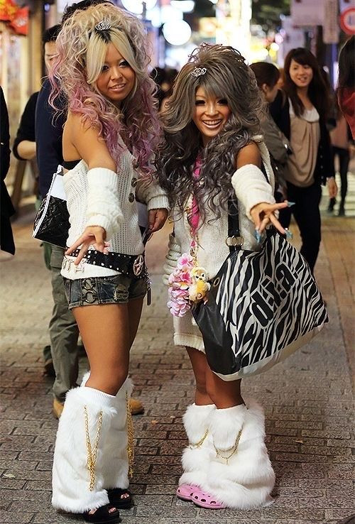 A group of young women showcasing vibrant gyaru fashion in an urban setting, highlighting their tanned skin, blonde hairstyles, and bold makeup, embodying the energetic and rebellious spirit of Japanese youth culture.