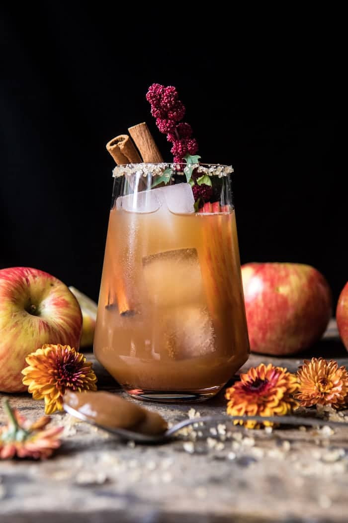 alt text: a close-up image of an apple butter old fashioned cocktail in a rocks glass, garnished with a cinnamon stick and apple slices.