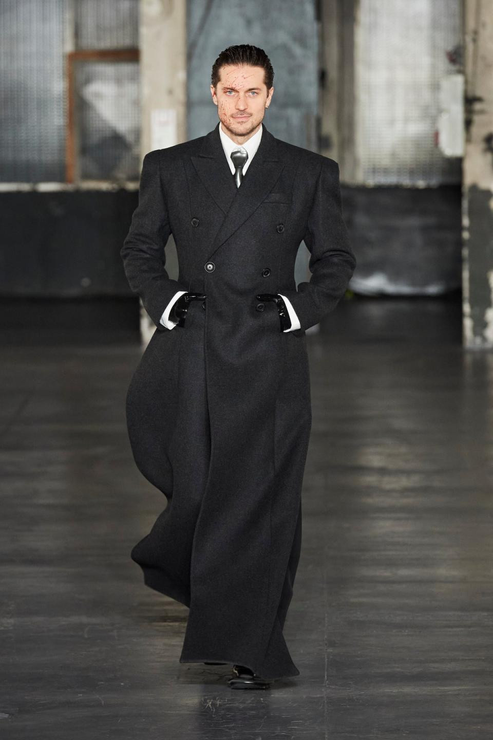 Lucas Bravo commands the runway at Paris Fashion Week Men's show, showcasing a bold grey overcoat and latex gloves, a striking look from the LGN collection.