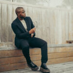 Man in black blazer and black jeans standing outdoors, showcasing a stylish urban look.