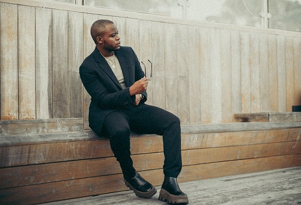 Man in black blazer and black jeans standing outdoors, showcasing a stylish urban look.