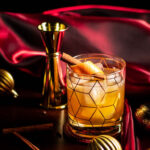 Christmas Old Fashioned in a rocks glass with an orange and cinnamon stick garnish.