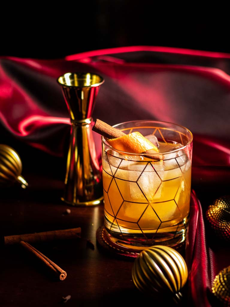 Christmas Old Fashioned in a rocks glass with an orange and cinnamon stick garnish.