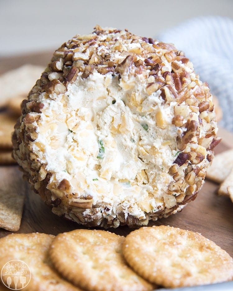 Close up image of a classic cheese ball rolled in nuts with crackers on a plate.