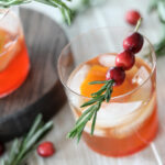 A cranberry old fashioned garnished with cranberries and rosemary.