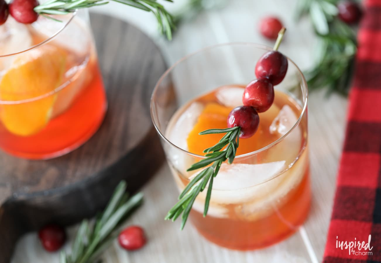 A cranberry old fashioned garnished with cranberries and rosemary.