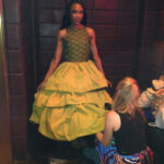 A model wearing a mustard yellow dress with a black lace bodice at Las Vegas Fashion Week.