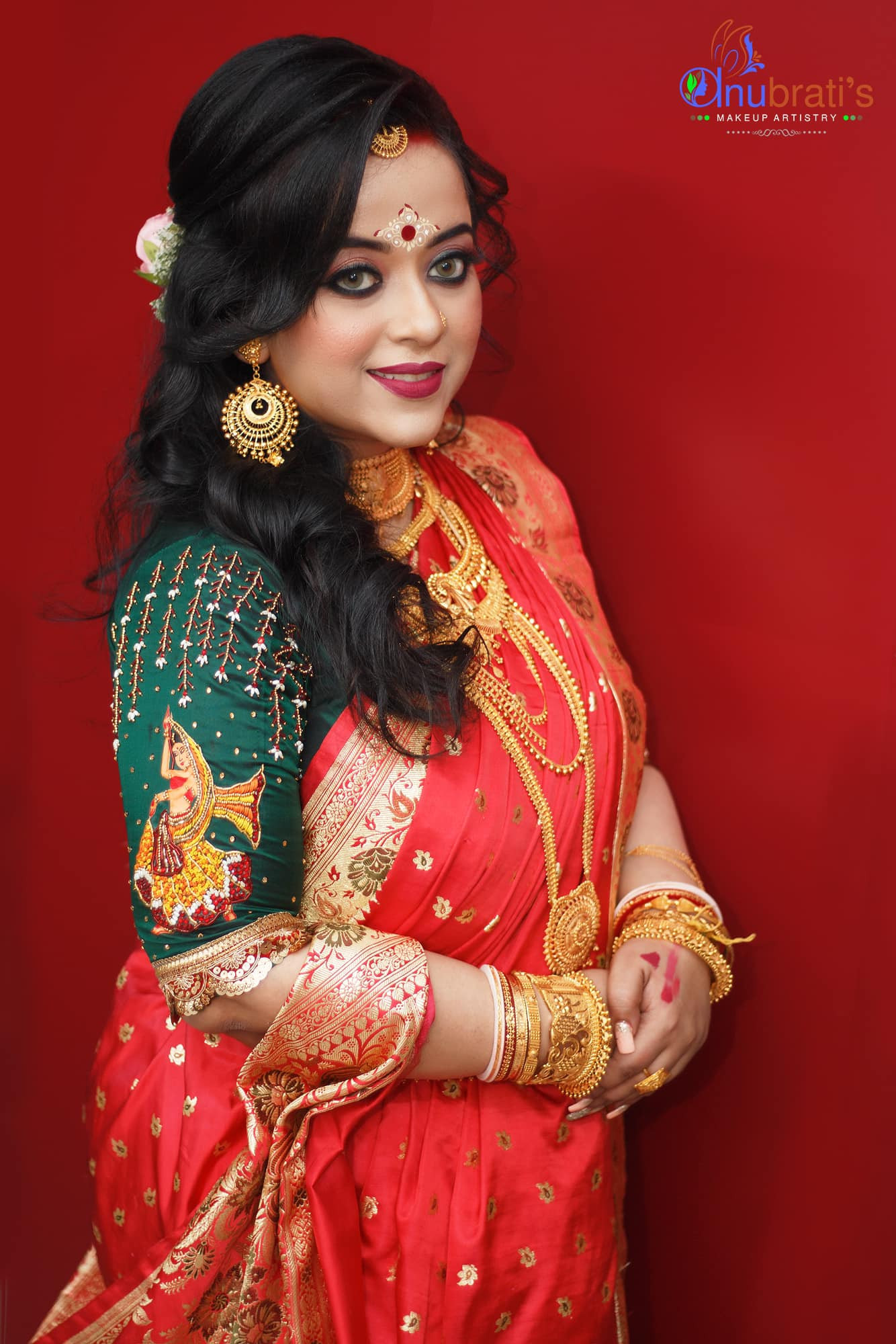 Bengali bride in a green portrait style blouse with red Banarasi saree, showcasing classic bridal elegance.