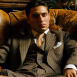 Suave man in Italian pinstripe suit, embodying classic mafia fashion, seated in leather chair.