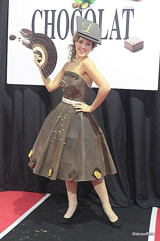 A model wearing a strapless chocolate dress decorated with chili peppers at a chocolate fashion show.