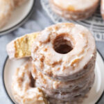 a stack of old fashioned donuts on a small white plate surrounded by more donuts