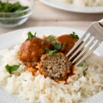 Porcupine meatballs on a plate of rice with a bite taken out of one of them.