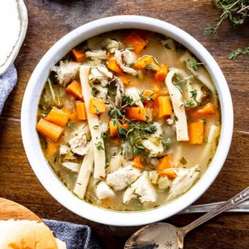 turkey carcass soup in a bowl together with herbs, spices, and bread on a wooden table