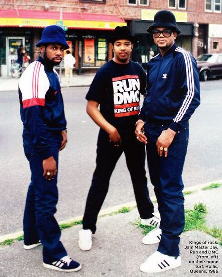 Run DMC wearing unlaced Adidas sneakers, leather jackets, and Kangol hats at a concert in 1986, showcasing their iconic street style and influence on hip-hop fashion.