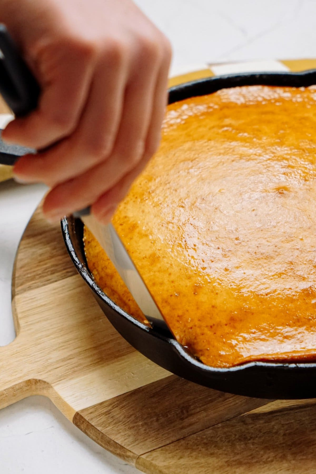 A person slicing a pineapple upside-down cake in a cast-iron skillet, showcasing the caramelized topping and moist cake interior.