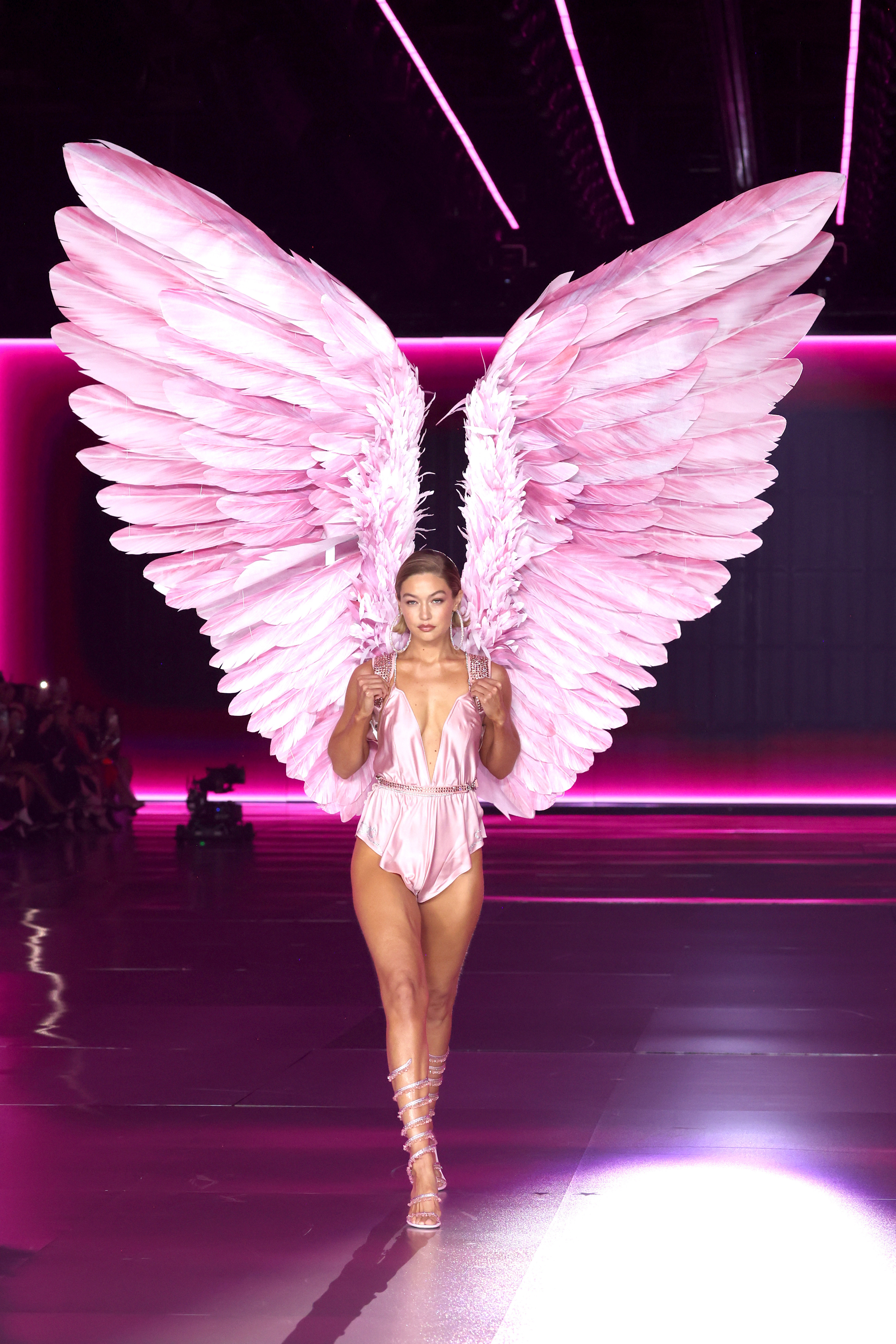 Gigi Hadid walks the runway for the Victoria's Secret Fashion Show 2024, wearing a satin pink bodysuit with crystal embellishments and large feathered wings