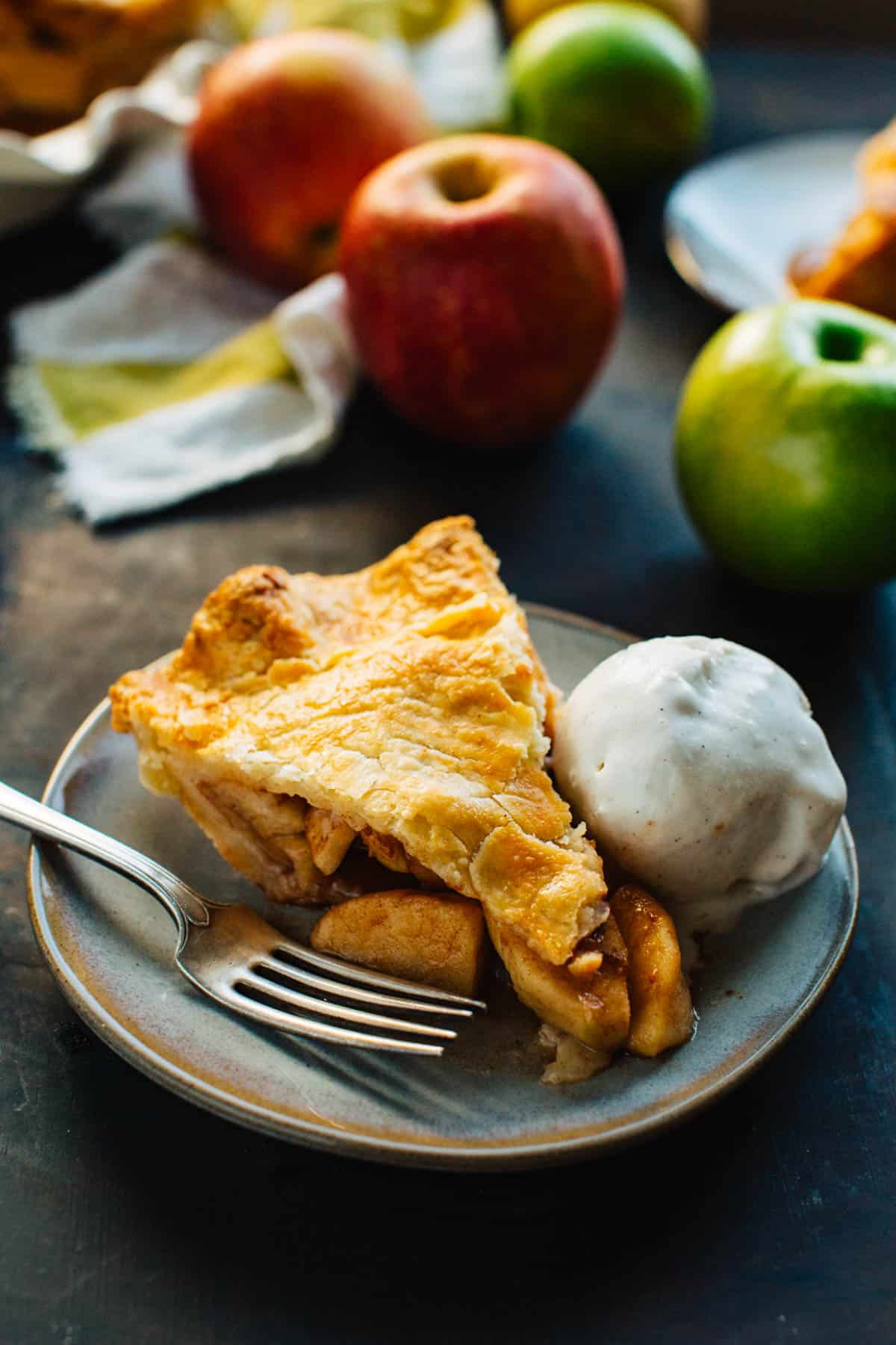 Slice of perfectly baked apple pie with a scoop of vanilla ice cream on a gray plate, showcasing its inviting texture and flavor