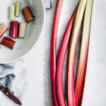 long stalks of fresh rhubarb next to a small knife and a bowl with rhubarb pieces