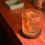 Man dressed in a tweed suit, holding a glass of scotch, embodying the old fashioned style, signifying timeless elegance and taste.