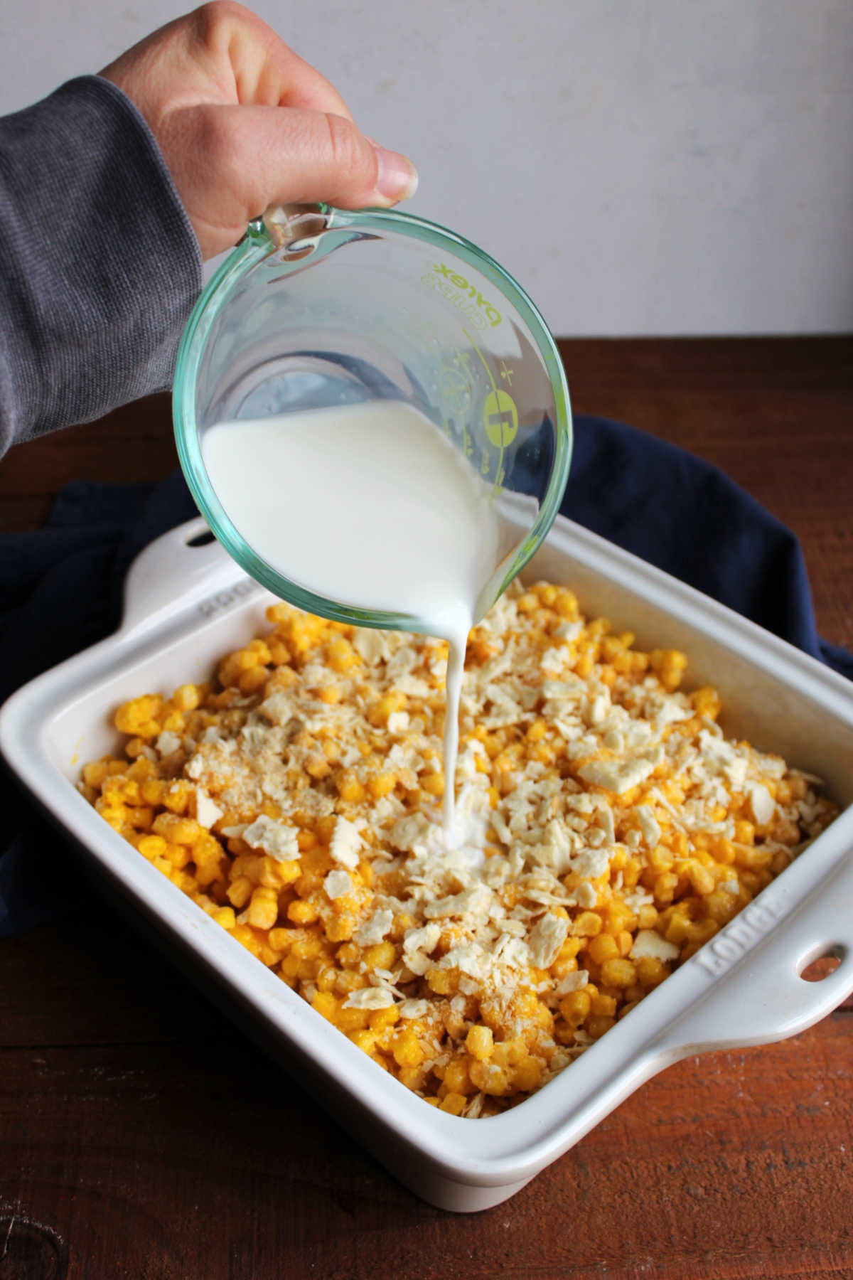 Pouring milk over the pan filled with corn, eggs, and cracker crumbs.