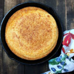 Golden brown cornbread cooling in a cast iron skillet.