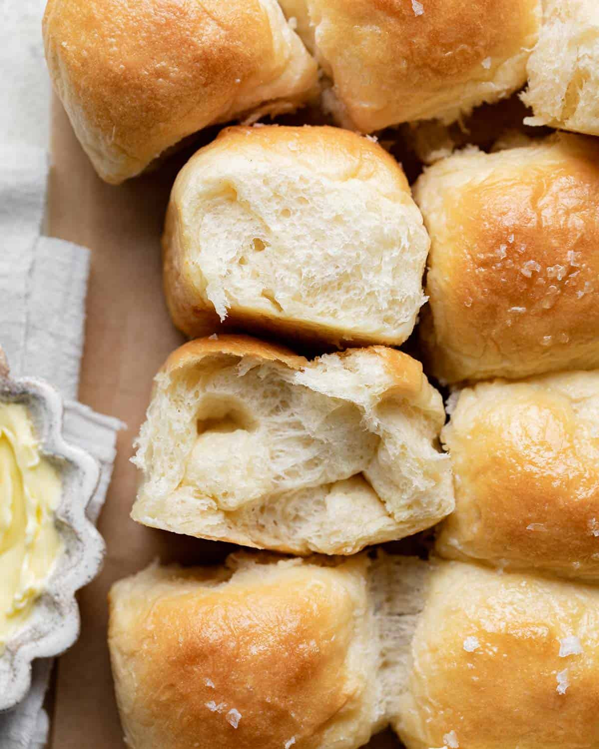 A basket filled with warm, golden-brown dinner rolls, accompanied by a small dish of butter, ready to be served.