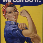 Woman wearing a khaki jacket and blue jeans, styled like Rosie the Riveter
