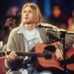 Kurt Cobain's look, a graphic tee layered under a shirt and beige cardigan