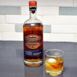 Bottled old fashioned next to a glass filled with whiskey and ice