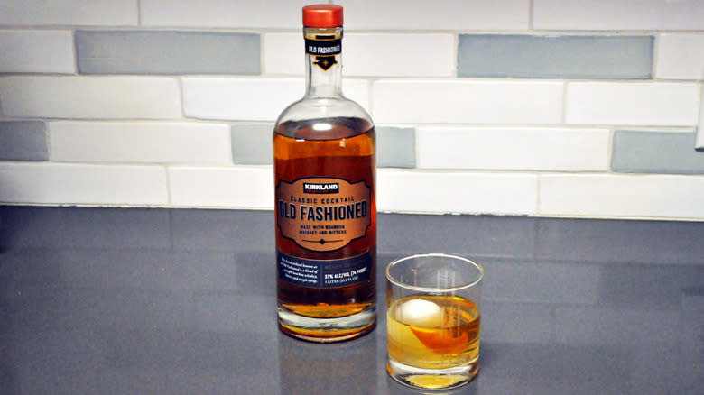 Bottled old fashioned next to a glass filled with whiskey and ice
