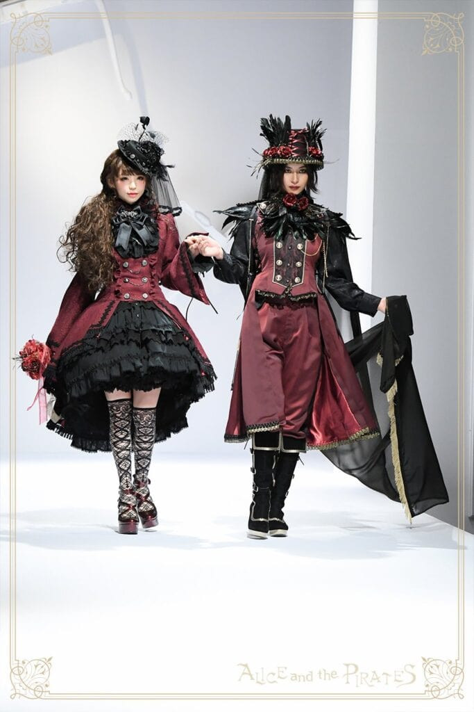 Two models, Midori Fukasawa and Akira, walking down the runway in matching red and black lolita and ouji sets by Alice and the Pirates.