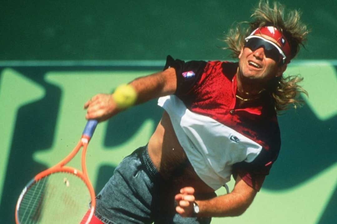Andre Agassi serving a tennis ball wearing shorts and mono-lens 80