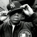 Jay-Z in 2000s hip-hop style, wearing a Roc-A-Fella chain and a fitted cap