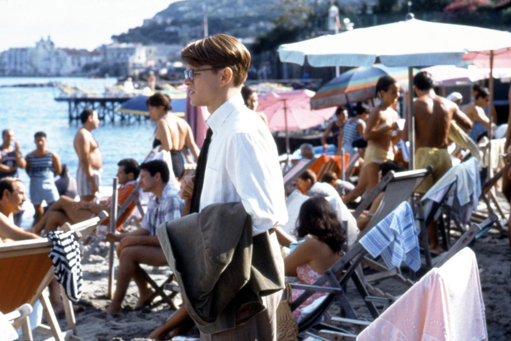 Matt Damon as Tom Ripley in Ivy League style attire, wearing a corduroy jacket, khaki chinos, and square glasses
