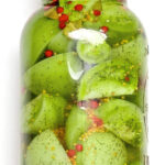A jar filled with sliced and pickled green tomatoes.