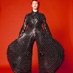 A black and white photo of David Bowie in a stripped bodysuit, showcasing an early example of anti-fashion pushing gender boundaries