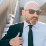Bald man in a tailored grey suit standing confidently