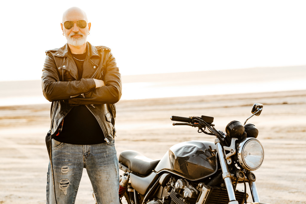 Bald man in a leather jacket with a motorcycle in the background