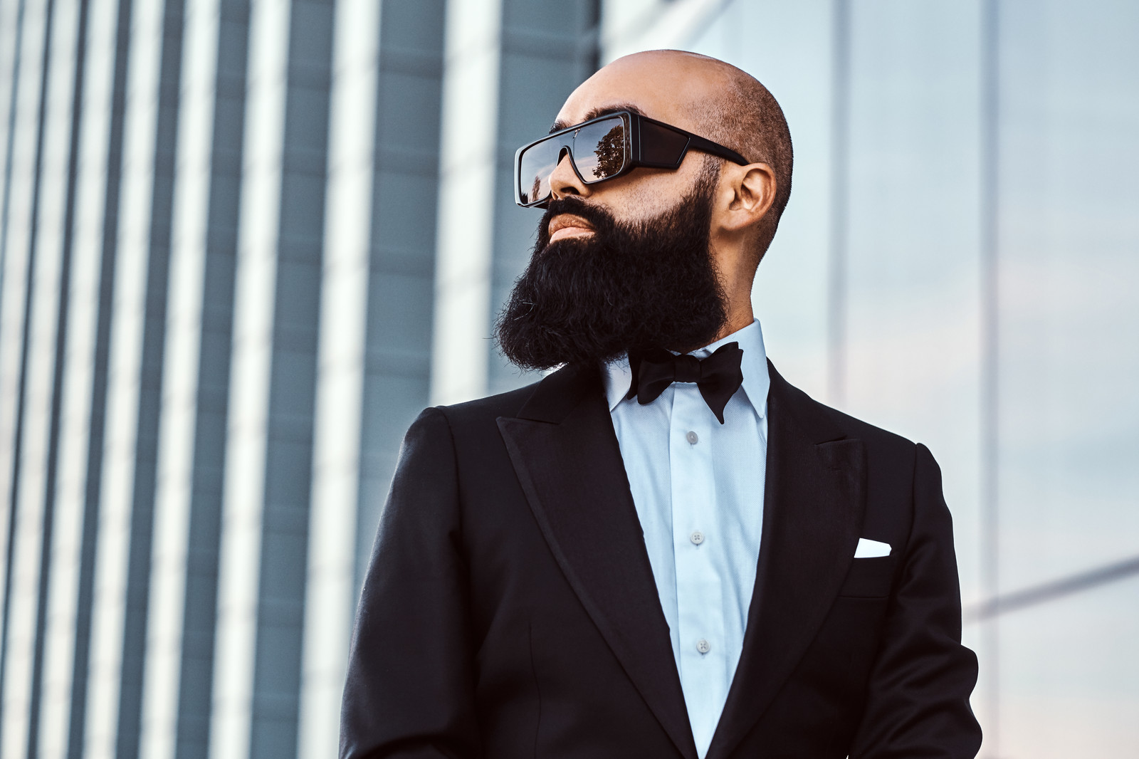 Man with a well-groomed beard in a black tuxedo and sunglasses