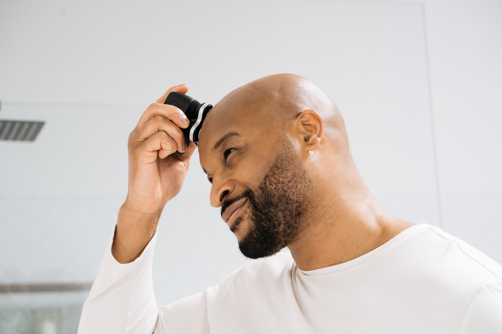Bearded bald man shaving his head with a razor
