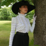 An Edwardian woman showcasing a white bloused bodice with intricate lace detailing, paired with a dark tailored skirt, exemplifying the era's refined simplicity and elegance.