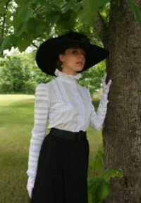 An Edwardian woman showcasing a white bloused bodice with intricate lace detailing, paired with a dark tailored skirt, exemplifying the era's refined simplicity and elegance.