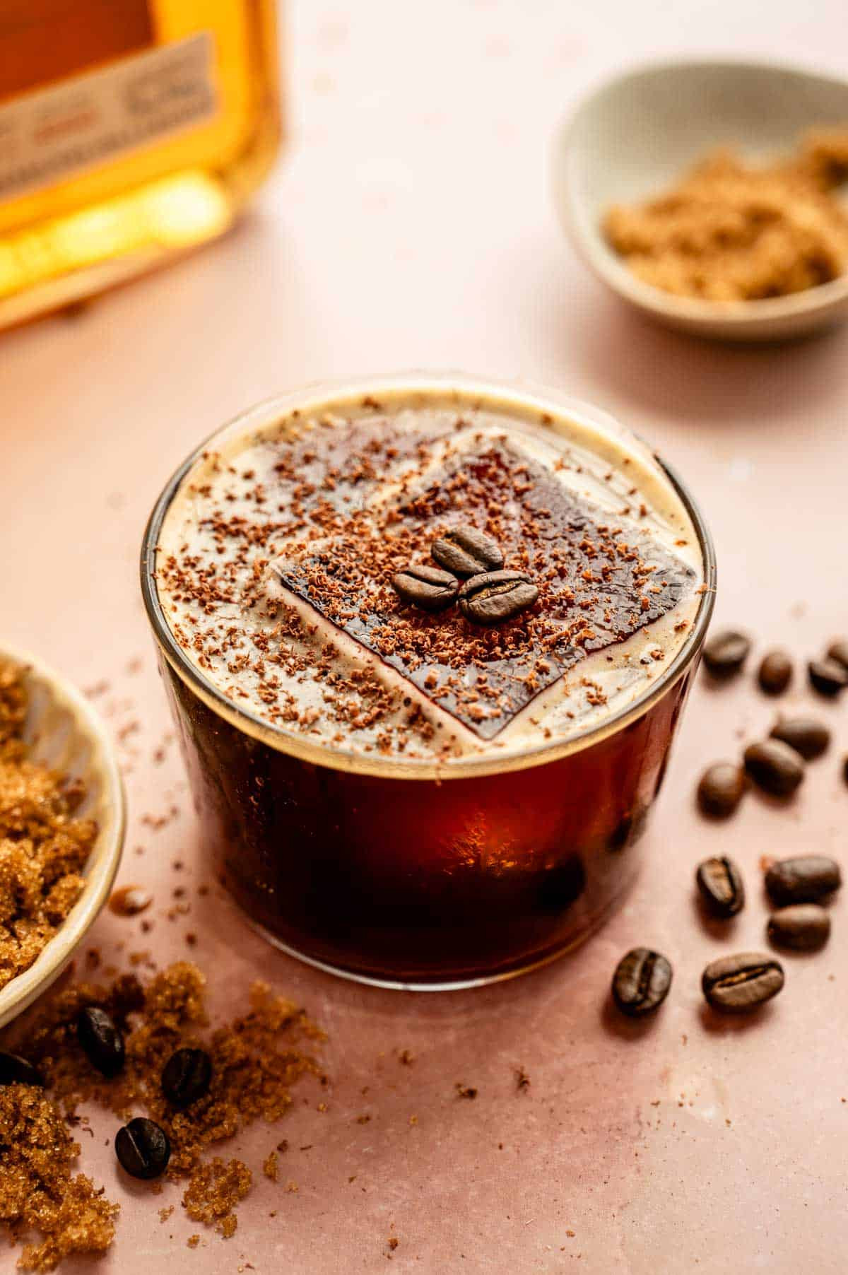 A Bourbon Espresso Old Fashioned garnished with coffee beans and chocolate shavings on a bar top
