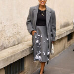 Woman in a beige A-line skirt, paired with a black top and sunglasses, standing outdoors