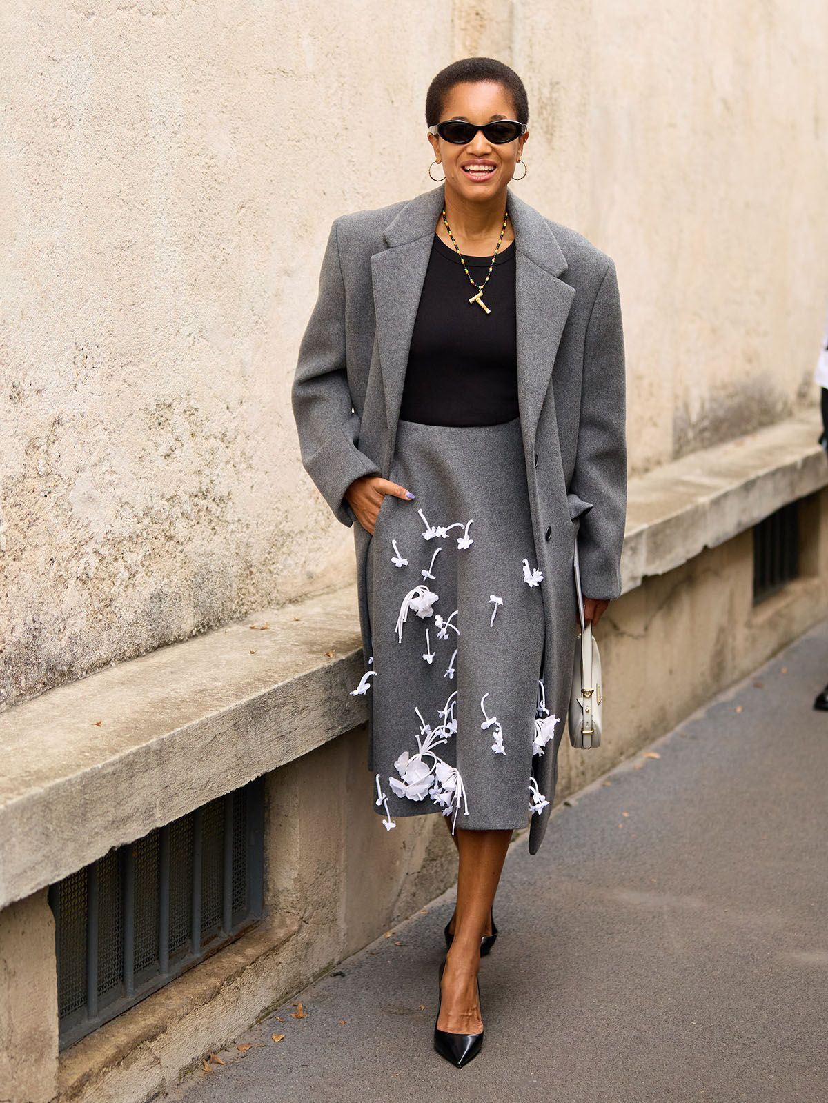 Woman in a beige A-line skirt, paired with a black top and sunglasses, standing outdoors