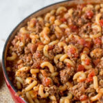 A close-up shot of goulash in a red pot, highlighting the melted cheese and rich sauce, evoking warmth and comfort