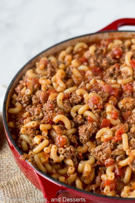 A close-up shot of goulash in a red pot, highlighting the melted cheese and rich sauce, evoking warmth and comfort