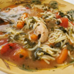 A bowl of chicken soup with spinach, carrots, and cut up spaghetti